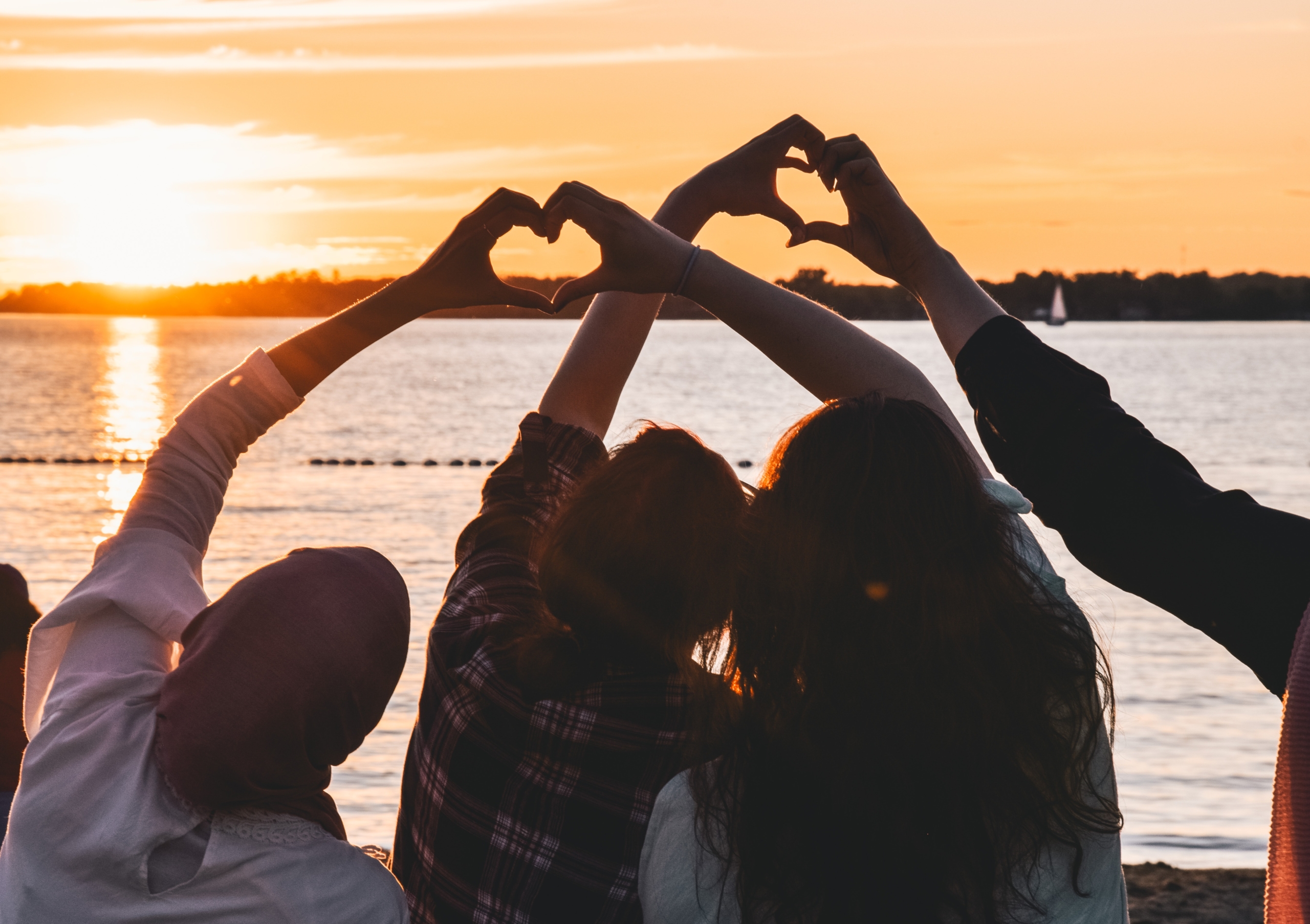 silhouette of friends looking at sunset, arms raised, making hearts with hands
